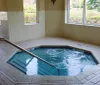 This is an indoor swimming pool area with a jacuzzi multiple lounge chairs and large windows allowing in natural light
