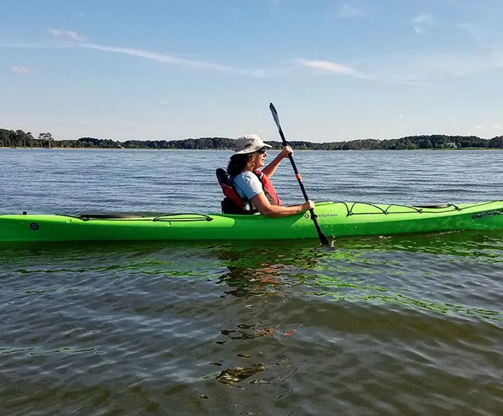 A person is kayaking on calm water under a clear blue sky