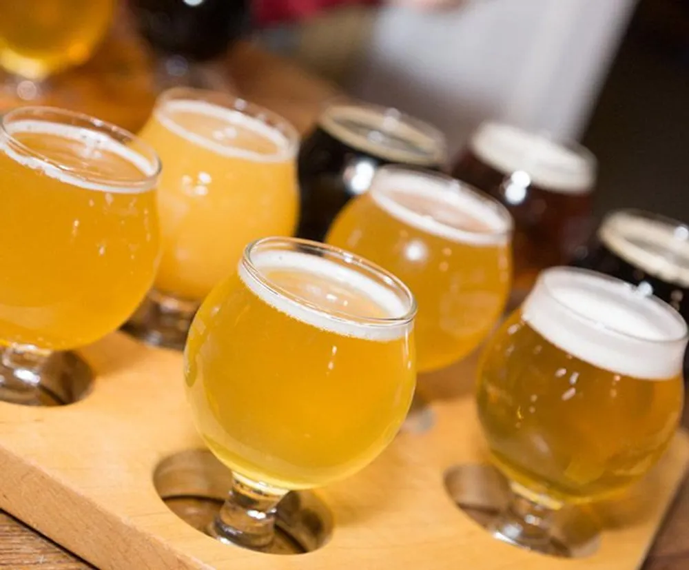 The image shows a wooden flight board with a selection of different colored craft beers in glasses ready for tasting
