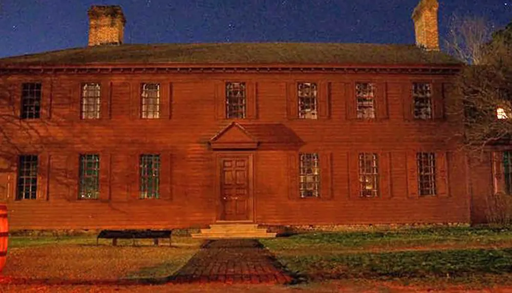 A large two-story red wooden house with multiple windows and chimneys is depicted at night adorned with shadows and warm lighting