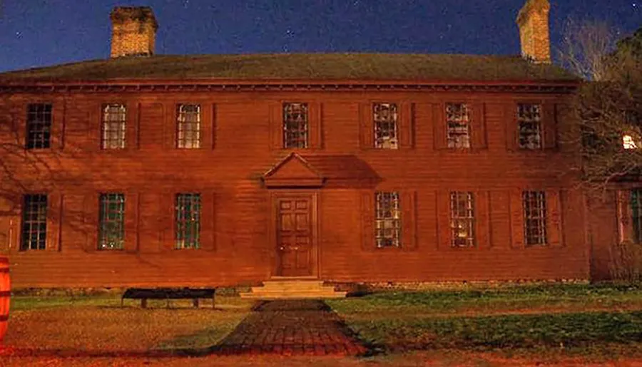 A large, two-story, red wooden house with multiple windows and chimneys is depicted at night, adorned with shadows and warm lighting.