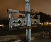 An old wooden pillory stands ominously in nightfall, perhaps a historic relic or a reproduction, typically used in the past for public humiliation and punishment.