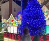 The image shows an elaborately decorated house for Christmas with numerous colorful lights inflatable characters and figures that create a festive and vibrant holiday scene