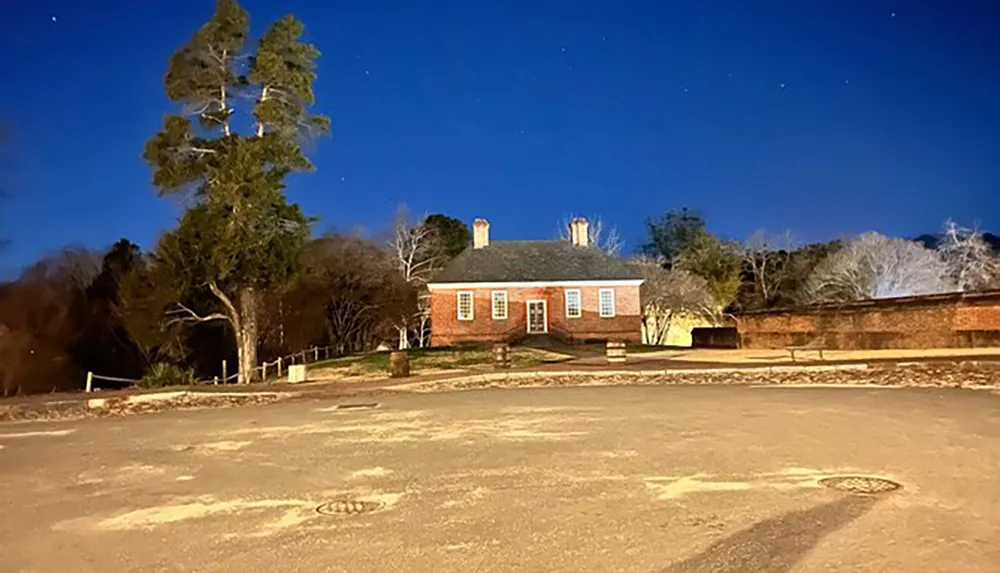 A colonial-style brick building is illuminated at twilight under a clear blue sky speckled with stars
