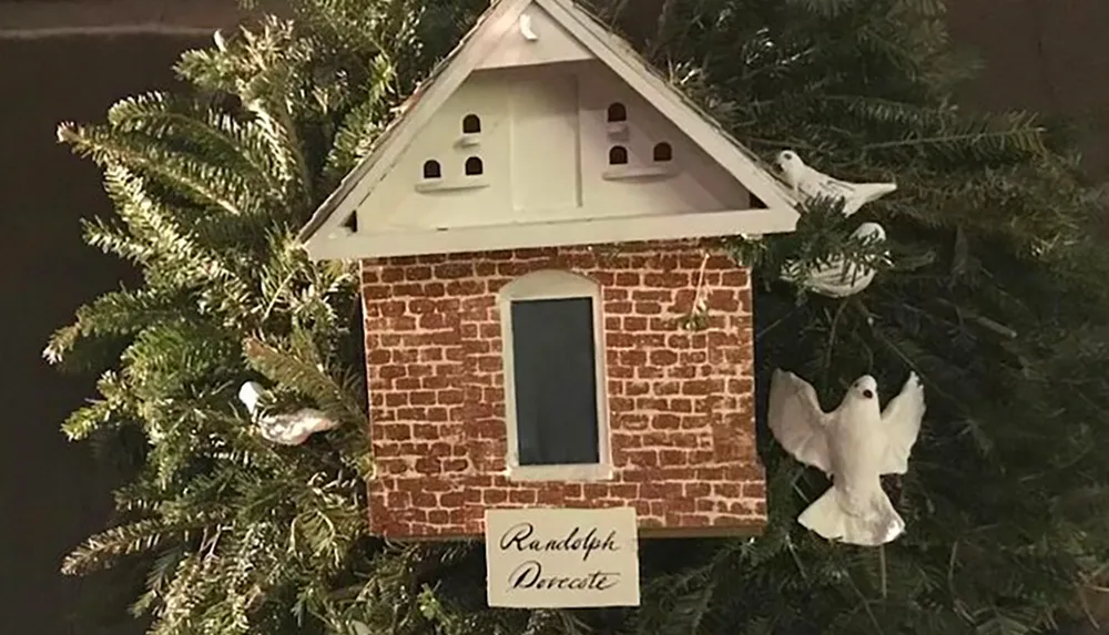 The image shows a decorative birdhouse with a brick facade attached to a tree accompanied by several bird ornaments and a sign reading Randolph Decorate
