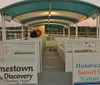 A ferry named Jamestown Discovery is cruising on the water with passengers on board during what appears to be late afternoon