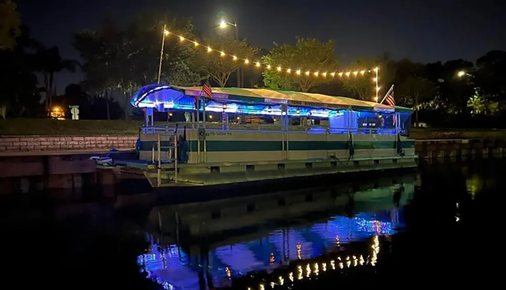 A boat decorated with lights is moored at a dock during the evening reflecting in the water
