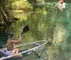 A group of individuals is kayaking in clear water with one person in a transparent kayak revealing the underwater view