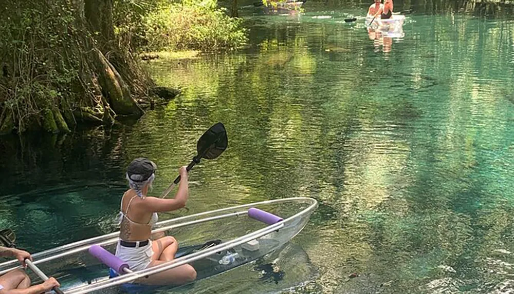 People are enjoying kayaking on a clear and serene blue waterway surrounded by greenery
