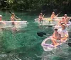 A group of individuals is kayaking in clear water with one person in a transparent kayak revealing the underwater view