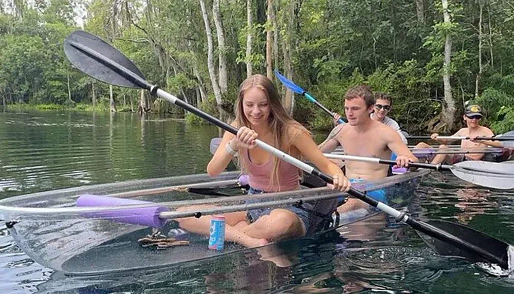 A group of individuals is kayaking in clear water with one person in a transparent kayak revealing the underwater view