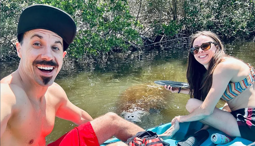 A smiling man and woman are enjoying kayaking together with a manatee visible in the water near them