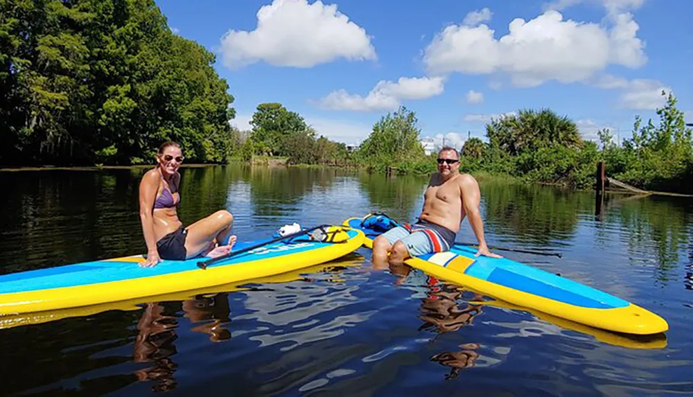 Two people are enjoying a sunny day on the water while sitting on their paddleboards