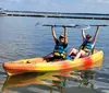 A group of people are standing on paddleboards in a waterway each holding a paddle aloft with a lush green backdrop and a bridge in the background