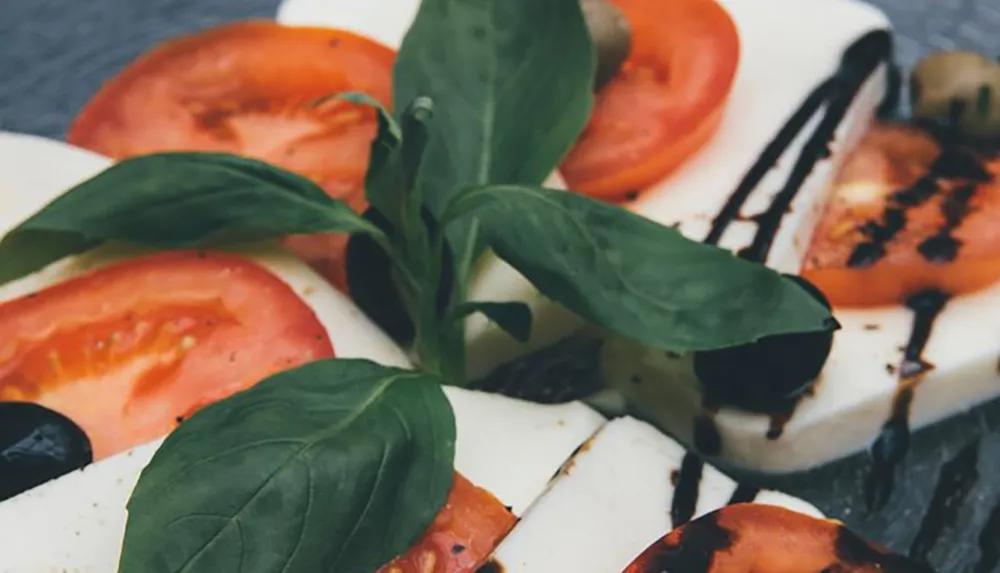 The image shows a Caprese salad with sliced tomatoes mozzarella cheese fresh basil and a balsamic glaze drizzle