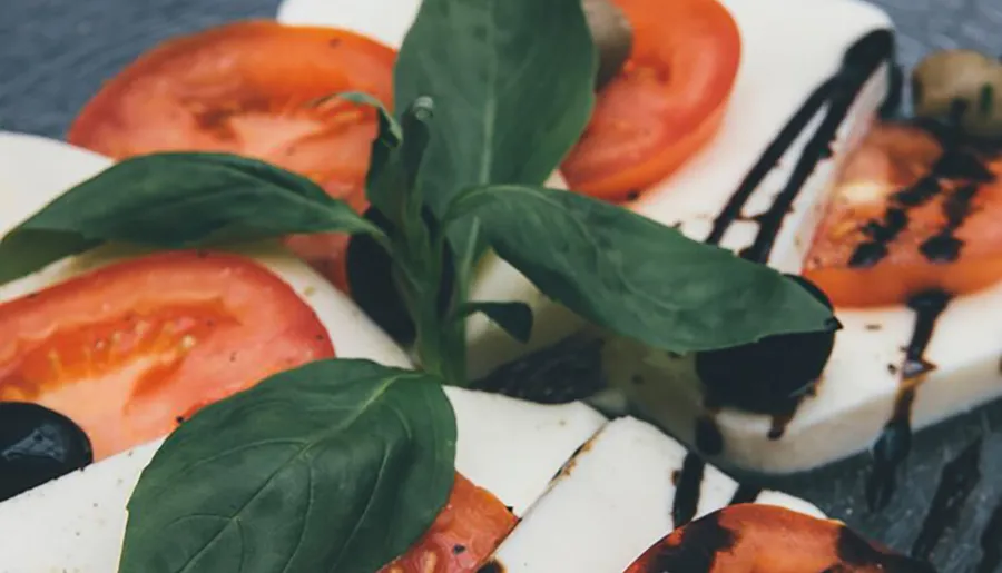 The image shows a Caprese salad with sliced tomatoes, mozzarella cheese, fresh basil, and a balsamic glaze drizzle.