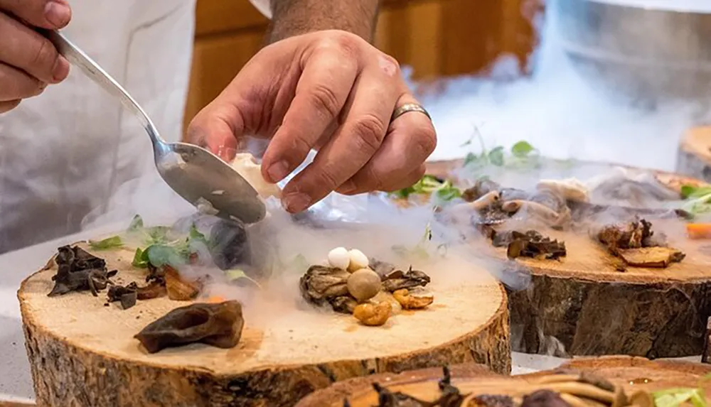 A chef is meticulously plating a dish with tweezers amid a smoky presentation on wooden surfaces suggestive of an upscale gourmet experience