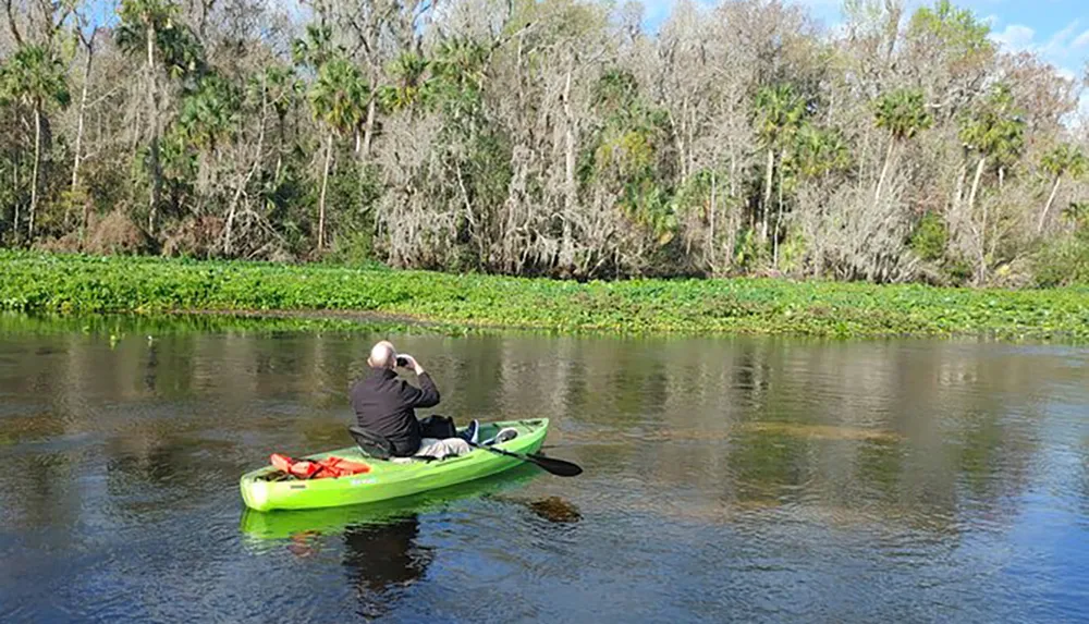 A person in a green kayak is paddling through a calm river surrounded by lush vegetation