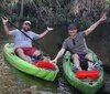 Two people are joyfully kayaking in a calm waterway surrounded by lush greenery