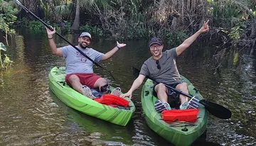 Two people are joyfully kayaking in a calm waterway surrounded by lush greenery.