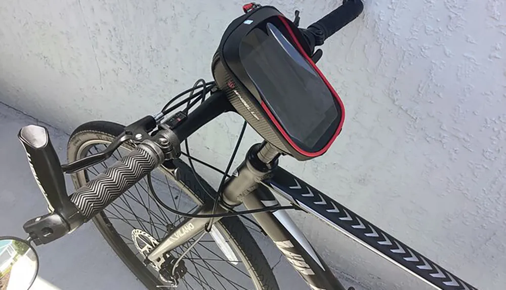 A bicycle is propped against a white wall with a smartphone mounted on its handlebars possibly for navigation or tracking purposes