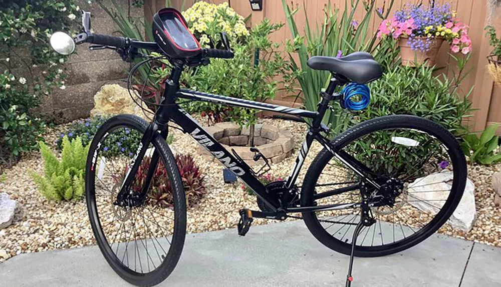 This image shows a black hybrid bicycle with the brand name written on the frame positioned outdoors with a garden and flowers in the background