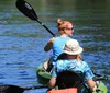 A person is kayaking on a clear and calm body of water surrounded by natural scenery