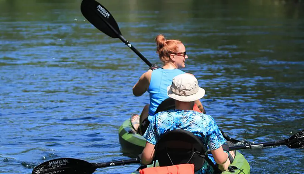 Two people are kayaking together on a calm river one paddling while the other sits in front