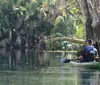 A person is kayaking on a clear and calm body of water surrounded by natural scenery