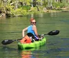 A person is kayaking on a clear and calm body of water surrounded by natural scenery