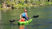 A person is kayaking on a clear and calm body of water surrounded by natural scenery.