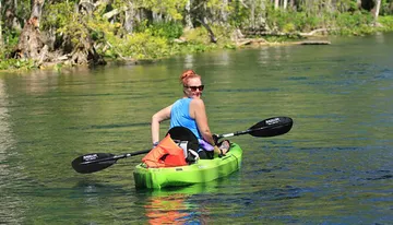 A person is kayaking on a clear and calm body of water surrounded by natural scenery.