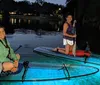 Four people are smiling and posing at night on a transparent canoe with underwater lighting that reveals the sea life below