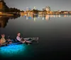 Four people are smiling and posing at night on a transparent canoe with underwater lighting that reveals the sea life below