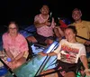 Four people are smiling and posing at night on a transparent canoe with underwater lighting that reveals the sea life below