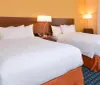The image shows a neatly arranged hotel room with two double beds warm lighting and a coordinating color scheme of blues and oranges