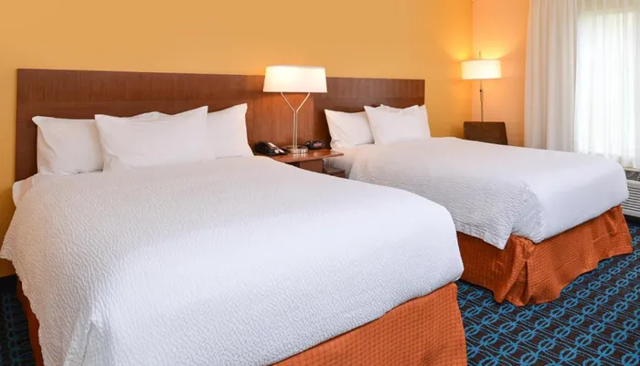 The image shows a neatly arranged hotel room with two double beds warm lighting and a coordinating color scheme of blues and oranges