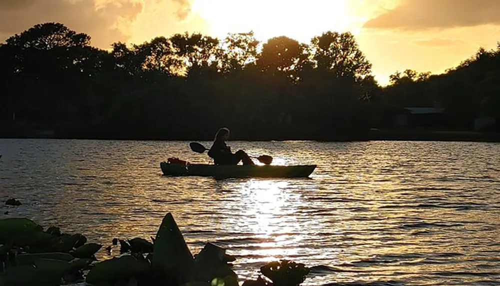 A person is kayaking on a tranquil lake against the backdrop of a sunset