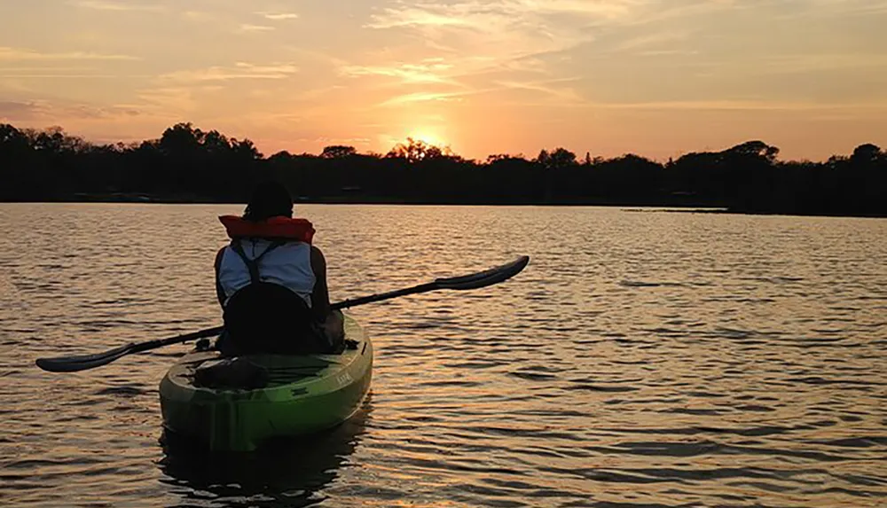 A person kayaks on calm waters against the backdrop of a beautiful sunset