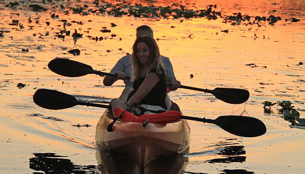 Two people are kayaking during sunset creating a silhouette against the waters reflective surface