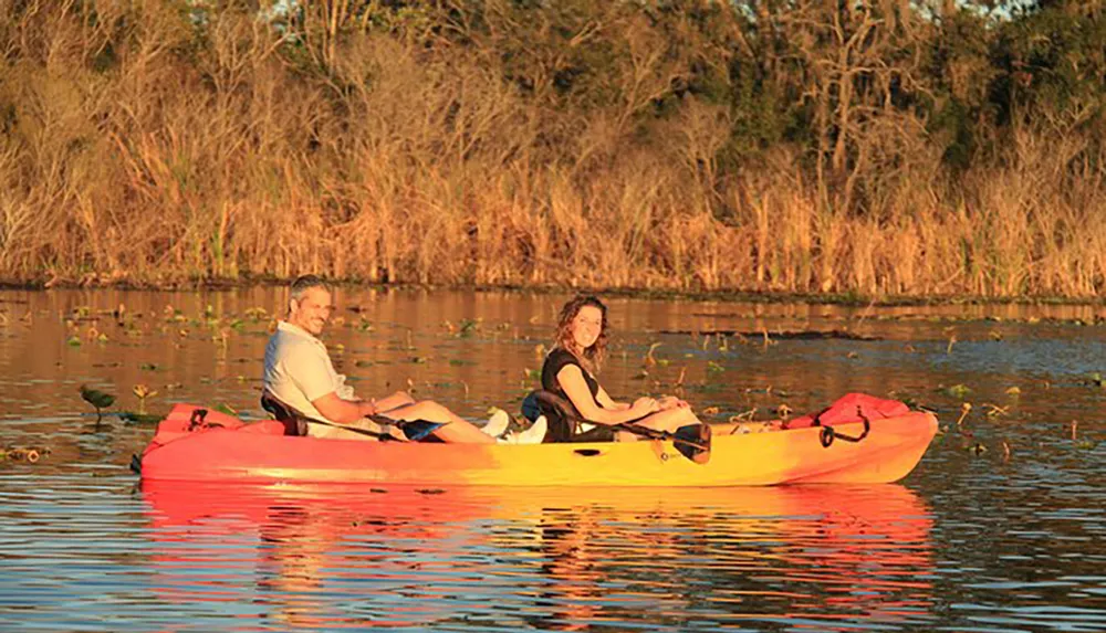 Two people are enjoying a kayak ride on calm waters during a warm golden hour