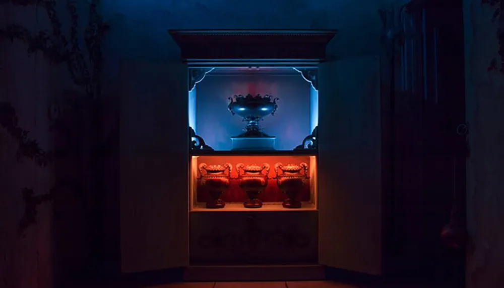 A dimly lit eerie room showcases an illuminated cabinet displaying ornate vases under a blue light on the top shelf and red light on the bottom creating a mysterious atmosphere