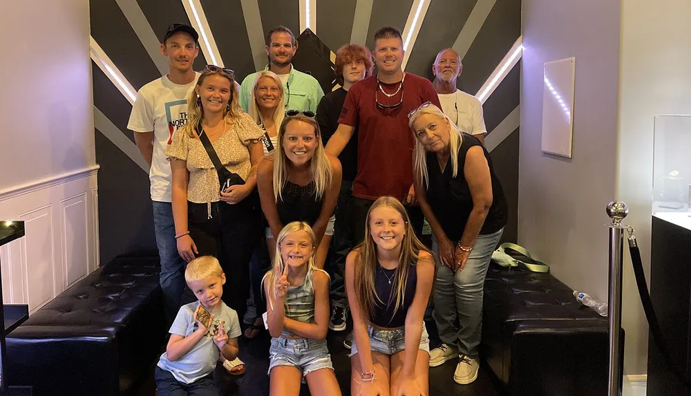 A group of eleven people of various ages are posing for a photo with smiles and casual poses taken in an indoor setting with a geometrically patterned backdrop