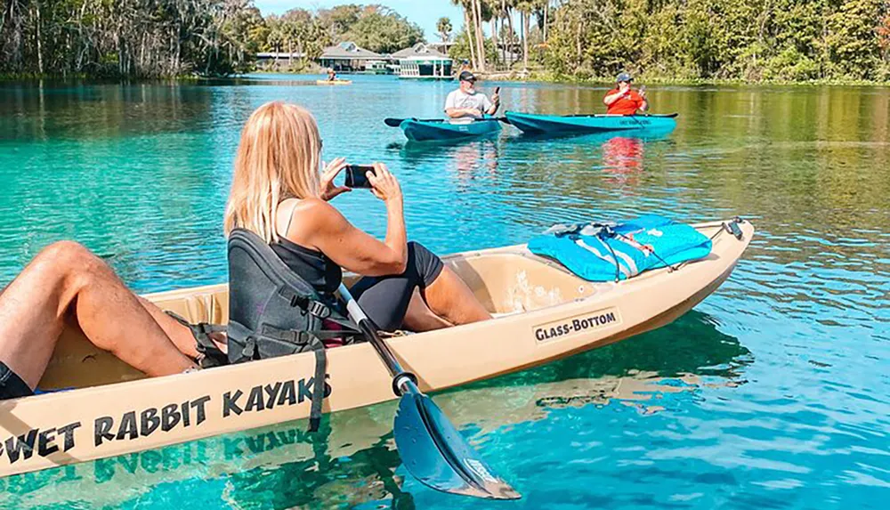 A person is taking a photo while kayaking in clear blue water along with other kayakers in the background
