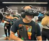 A group of people equipped with virtual reality headsets and gear are ready for an immersive VR experience in a facility with vibrant graphics on the walls and floor