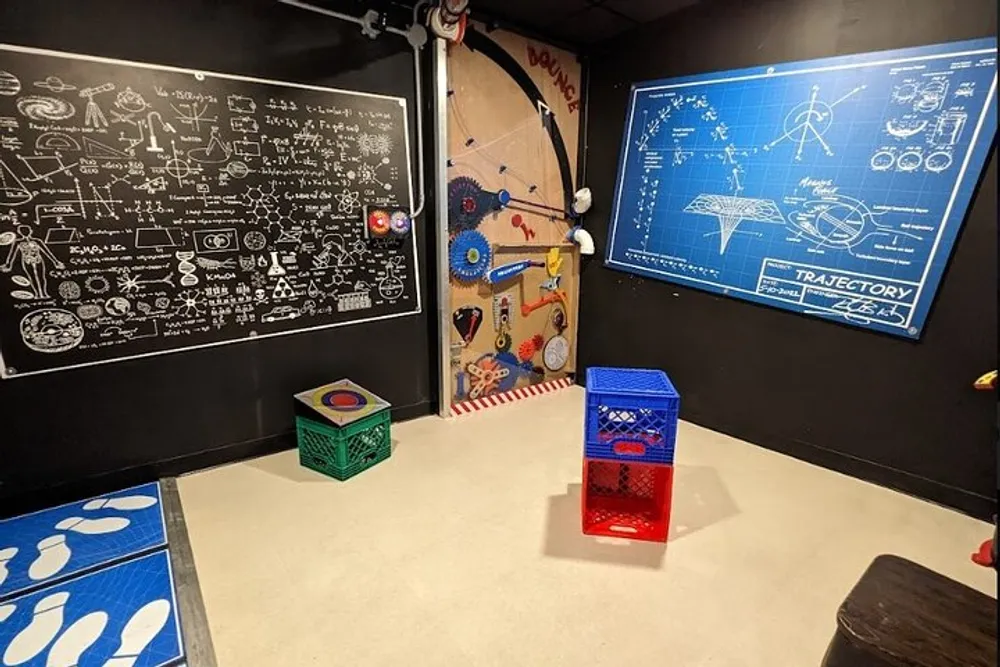 The image shows a themed escape room with science and engineering-inspired decor including chalkboard walls with equations a dartboard and a pegboard with gears