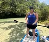 Two people are enjoying paddleboarding on a calm river surrounded by lush greenery on a sunny day