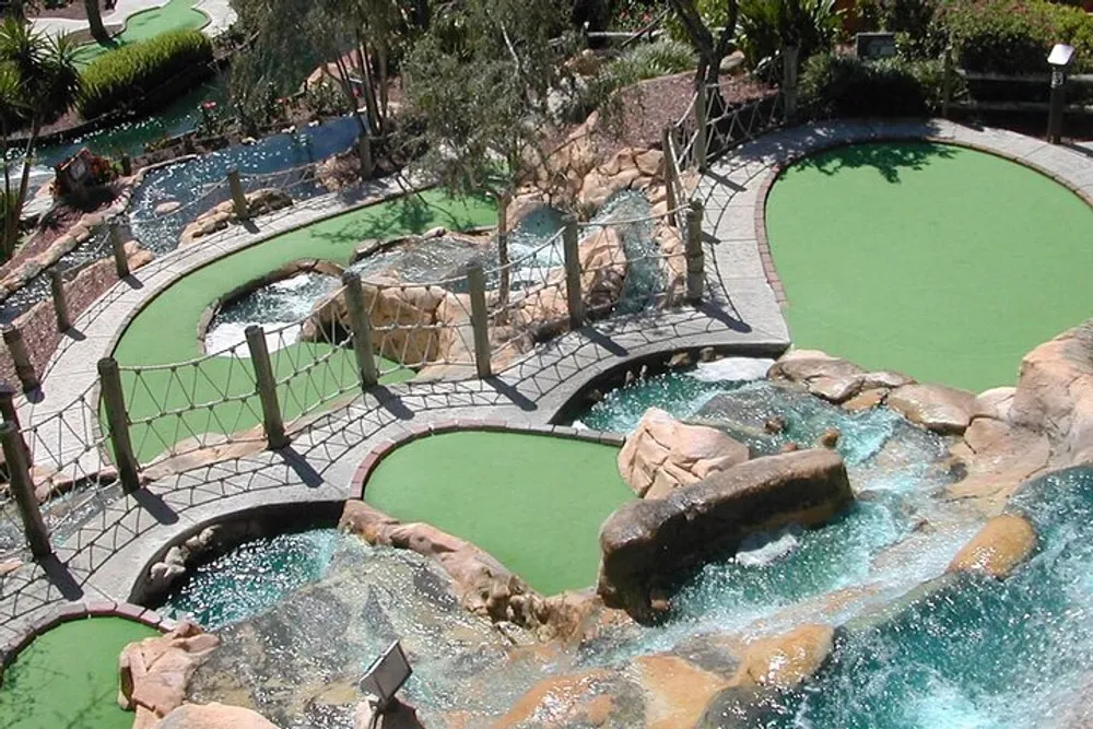 This image shows an aerial view of a miniature golf course with lush green artificial turf surrounded by decorative rocks and water features