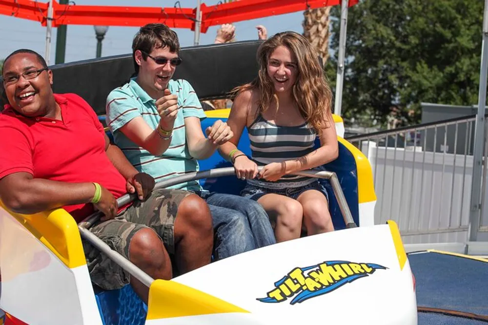 Three people are sharing a joyous moment on a Tilt-A-Whirl amusement park ride on a sunny day