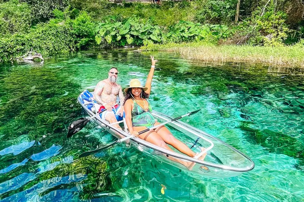 Two people are enjoying a clear kayak ride on a beautiful crystalline body of water surrounded by lush greenery